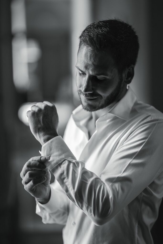 Portrait en noir et blanc d'un homme barbu en chemise blanche qui ajuste la manchette de sa chemise.