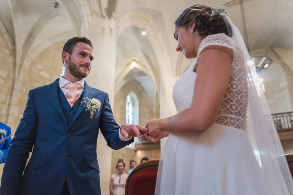 Le marié passe l'alliance au doigt de la mariée, devant les voûtes en pierre d'une église.
