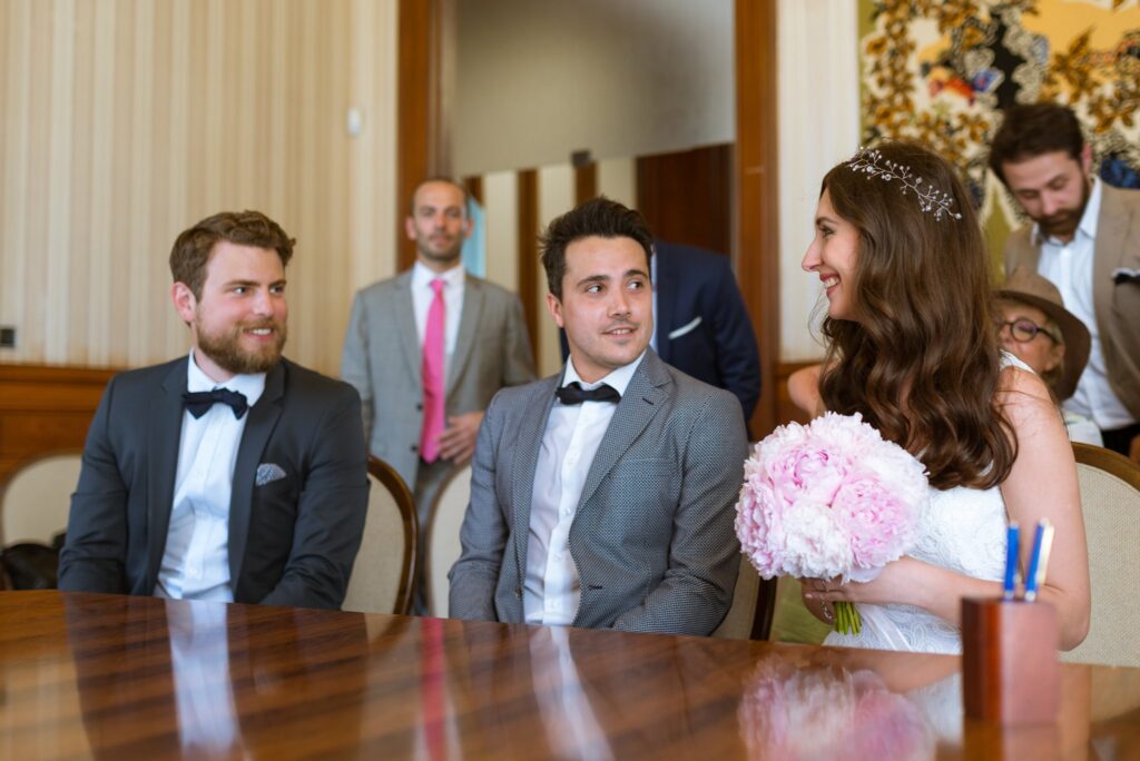 Les mariés sont assis à la table de la salle des mariages, entourés de témoins.