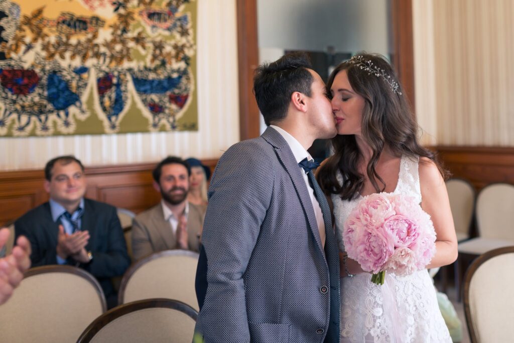 Le marié embrasse la mariée sur la joue pendant la cérémonie, devant les invités assis.