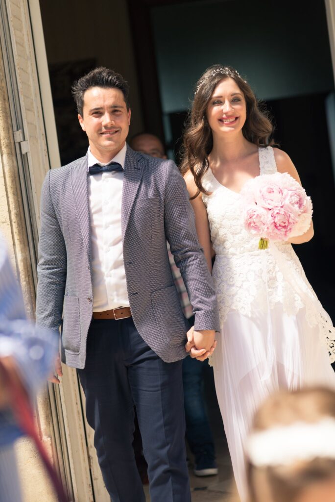Les mariés sortent de la mairie en se tenant la main, le bouquet de pivoines roses dans la main de la mariée.