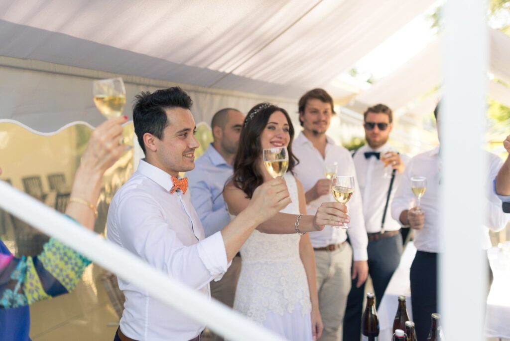 Sous une tente blanche, des invités et la mariée lèvent leur verre pour un toast.