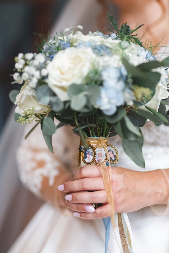 Gros plan sur le bouquet bleu et blanc d'une mariée, orné de petits médaillons photo.