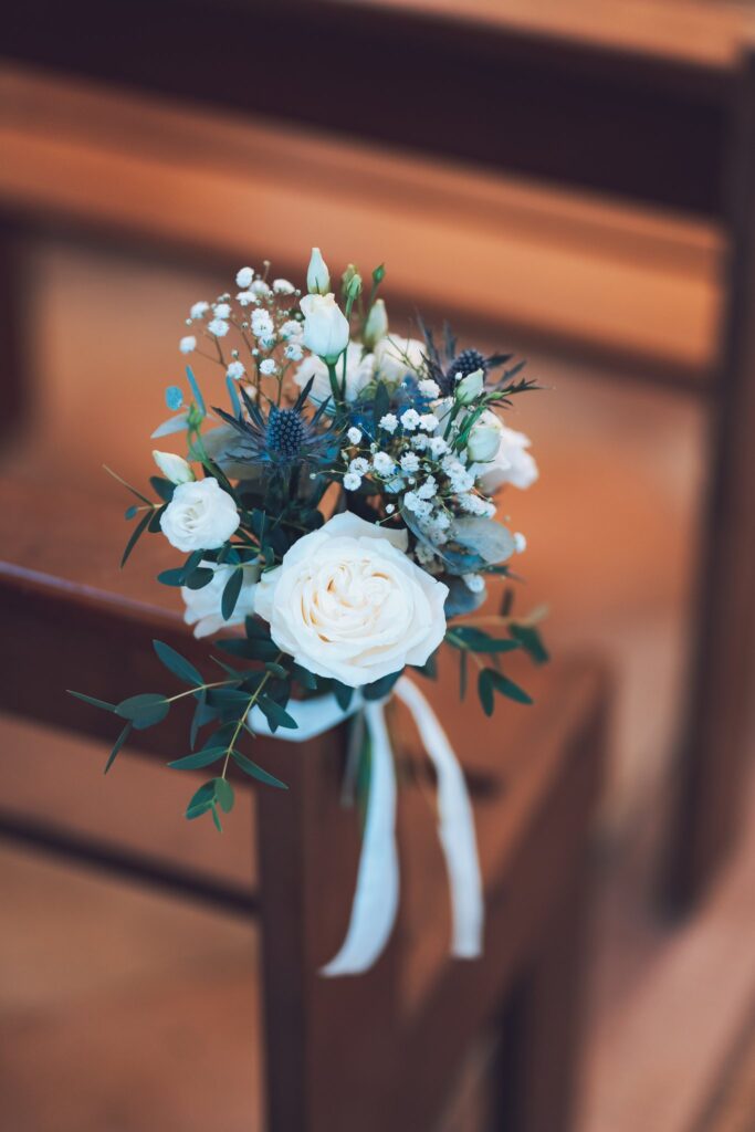 Un bouquet de fleurs blanches et bleues noué d'un ruban, accroché à un banc d'église en bois.