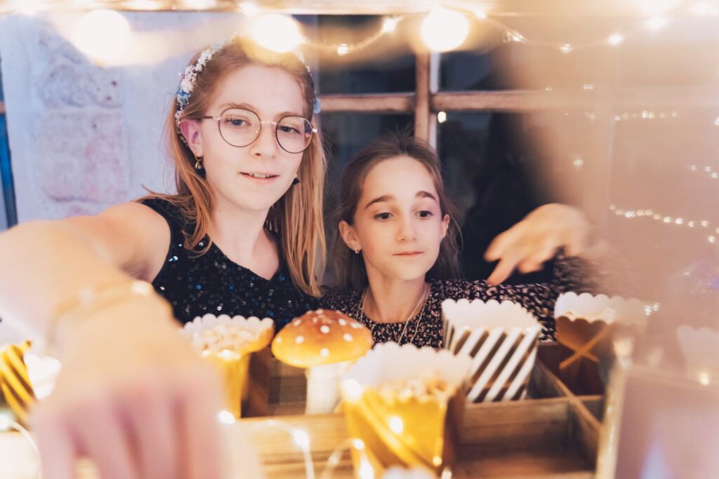 Deux jeunes filles choisissent des friandises sur un présentoir, sous des guirlandes lumineuses.