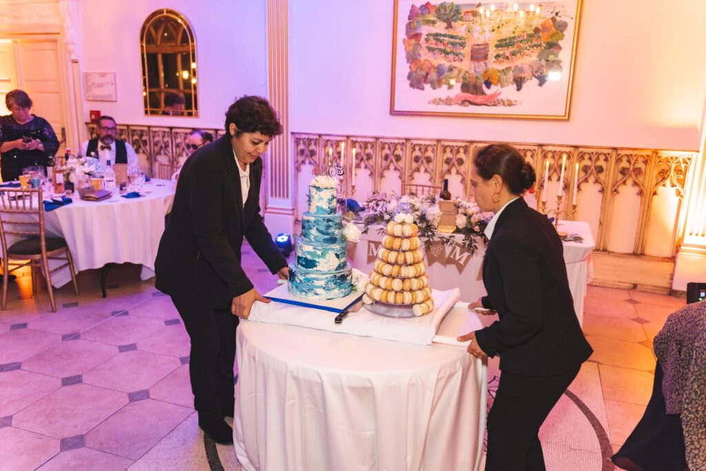 Deux personnes préparent le gâteau de mariage et une pièce montée de macarons dans une salle éclairée en rose.