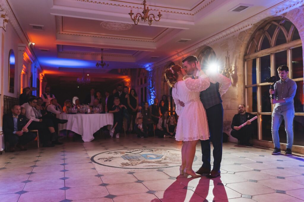 Un couple danse au centre d'une salle éclairée de lumières bleues et orangées, sous le regard des invités.