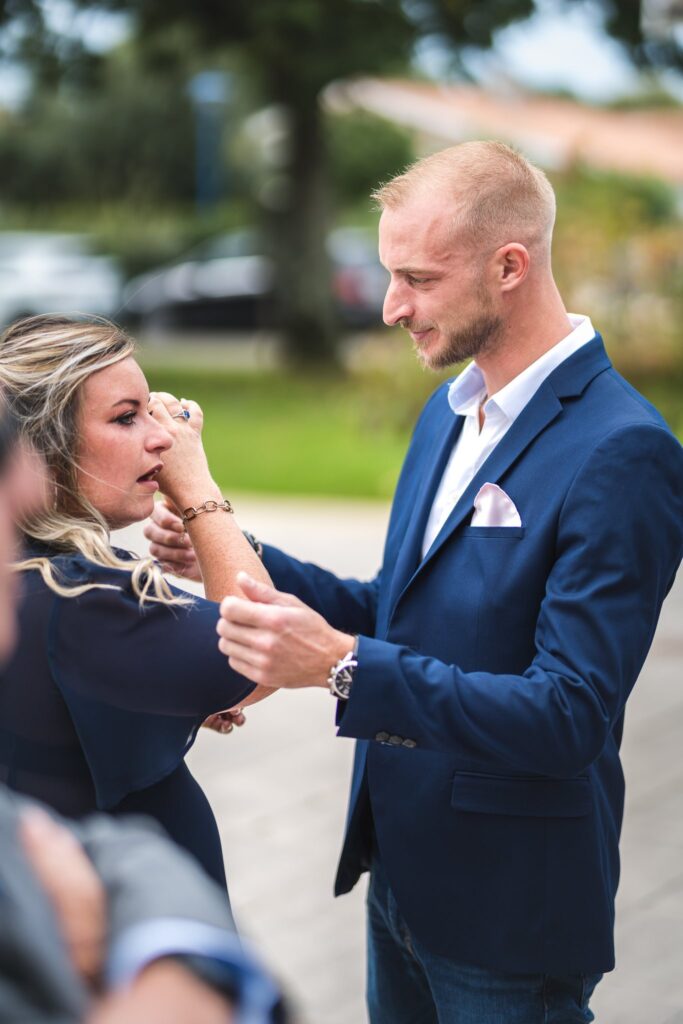 Une femme ajuste la manche d'un homme en veste bleu marine, en extérieur.