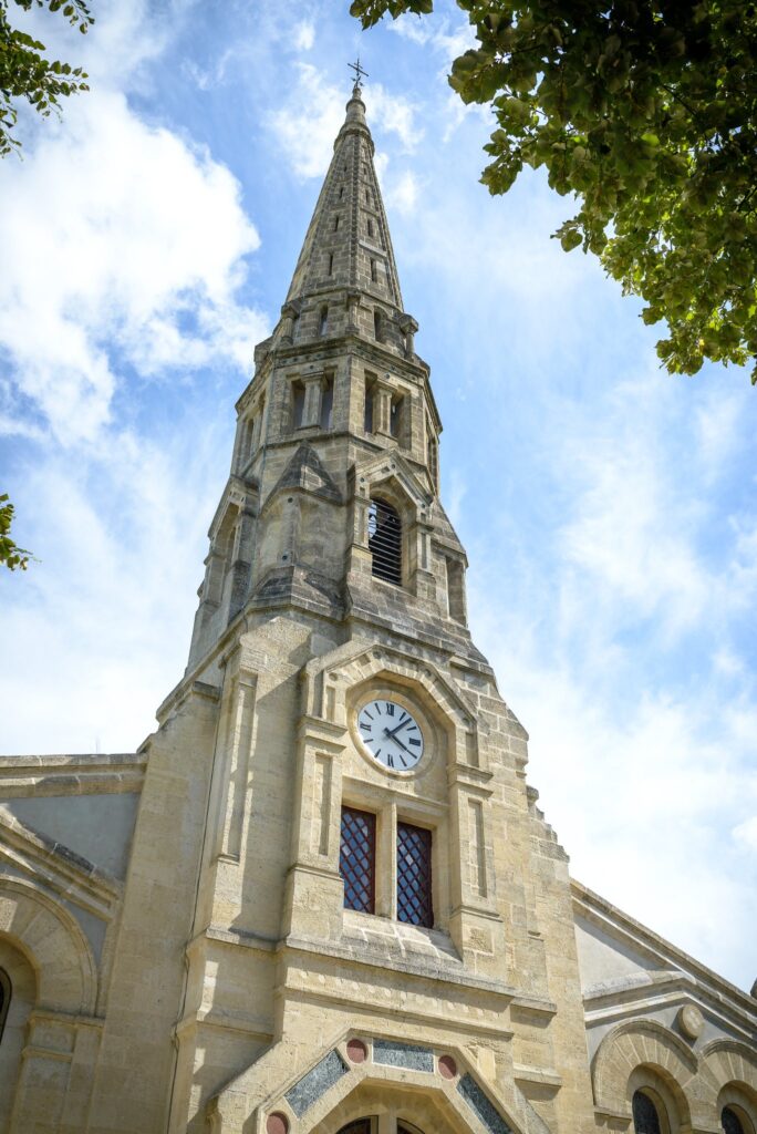Le clocher de l'église de Sauternes sous un ciel bleu, vu d'en bas à travers le feuillage.