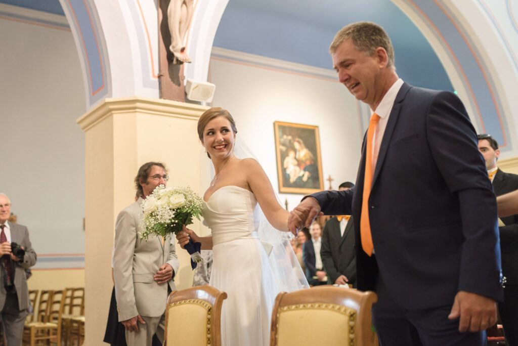 La mariée tenant son bouquet donne la main à un homme en costume dans l'allée de l'église.