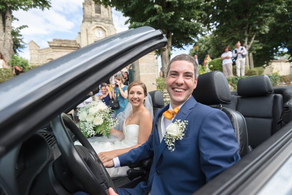 Le marié sourit au volant d'un cabriolet, la mariée assise à côté de lui.