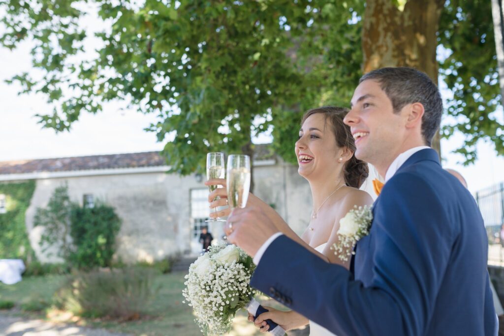 Les mariés lèvent leur verre dans un jardin, une bâtisse en pierre derrière eux.