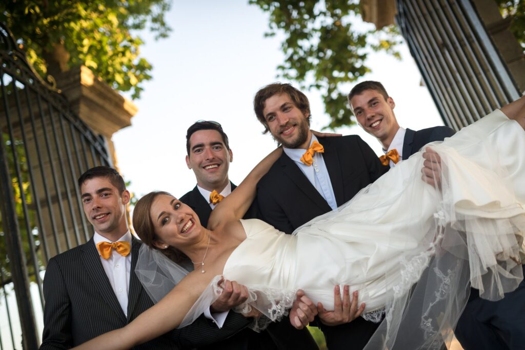 Des hommes en nœud papillon orange portent la mariée dans leurs bras.