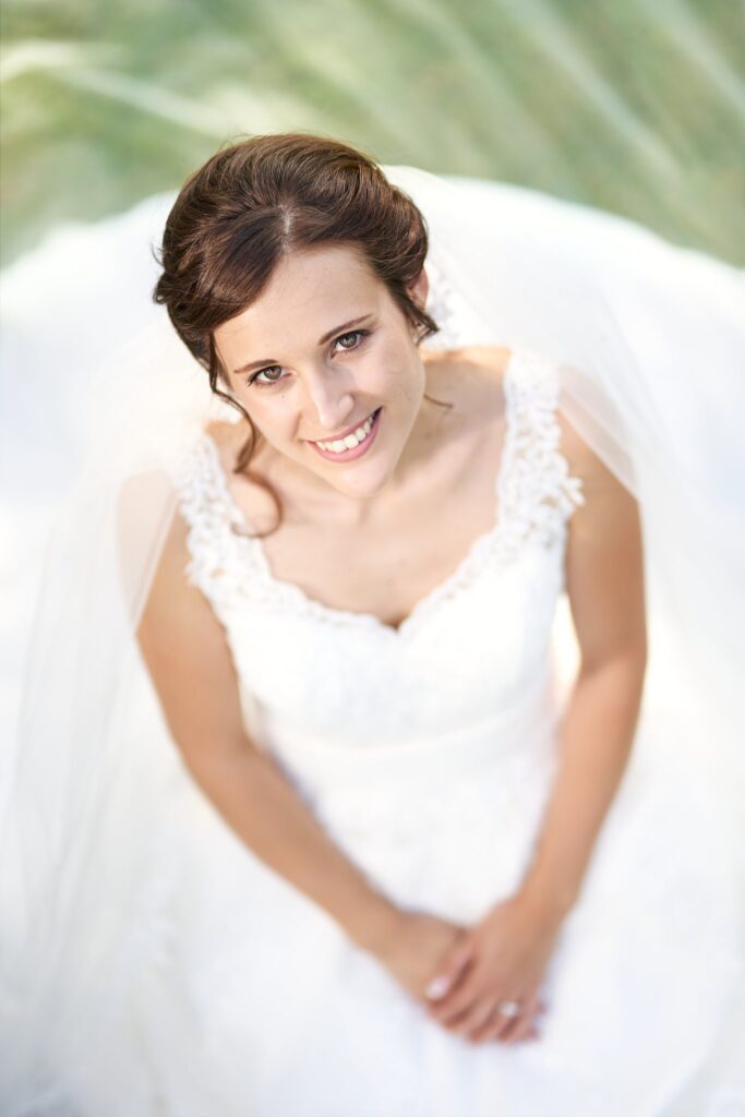 Vue en plongée d'une mariée souriante en robe blanche et voile, qui lève les yeux vers l'objectif.