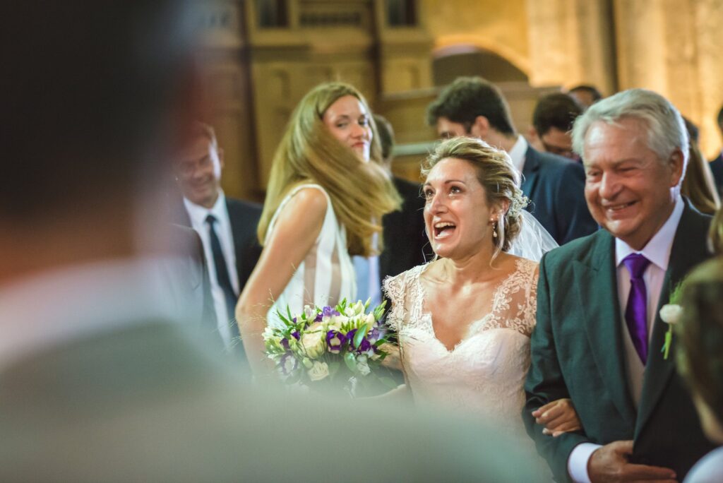 Une mariée rit en entrant dans l'église au bras d'un homme aux cheveux gris.