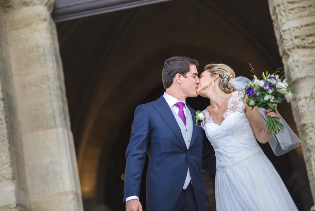 Les mariés s'embrassent à l'ombre du portail de la collégiale, le bouquet à la main.