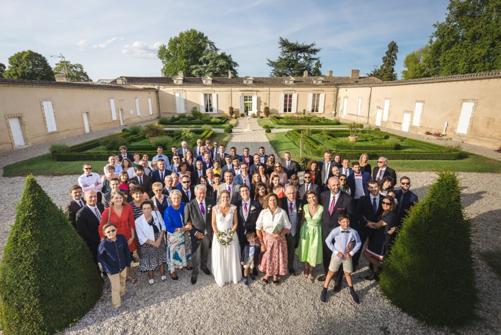 Photo de groupe des invités dans les jardins à la française d'un château, sous un ciel clair.