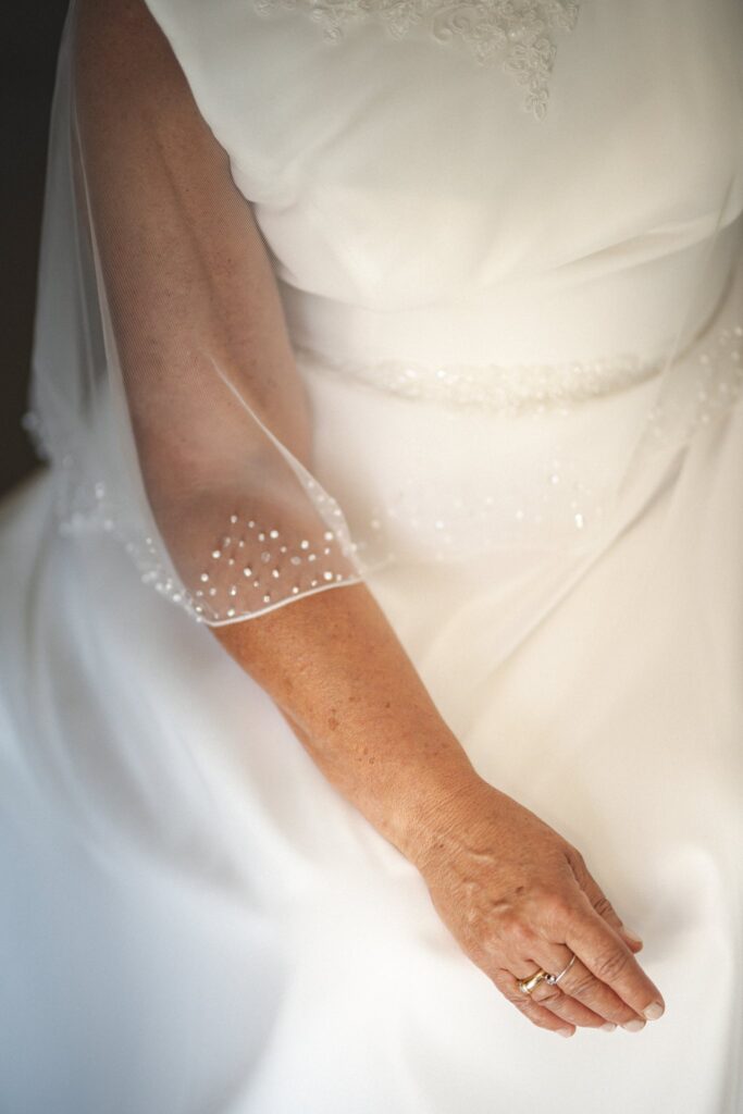Gros plan sur la main d'une mariée en robe blanche à manches brodées, avec son alliance.