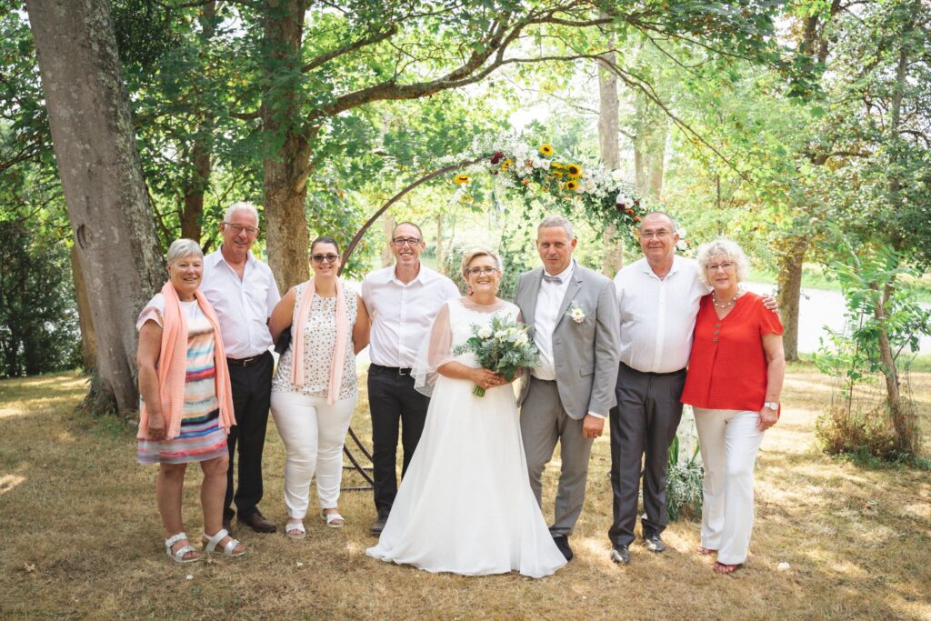 Les mariés entourés de plusieurs invités, en rang sous les arbres.