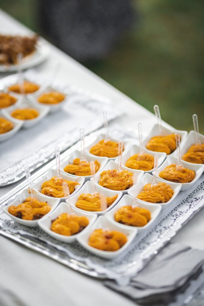 Des verrines de purée orange alignées sur un plateau argenté posé sur une table.