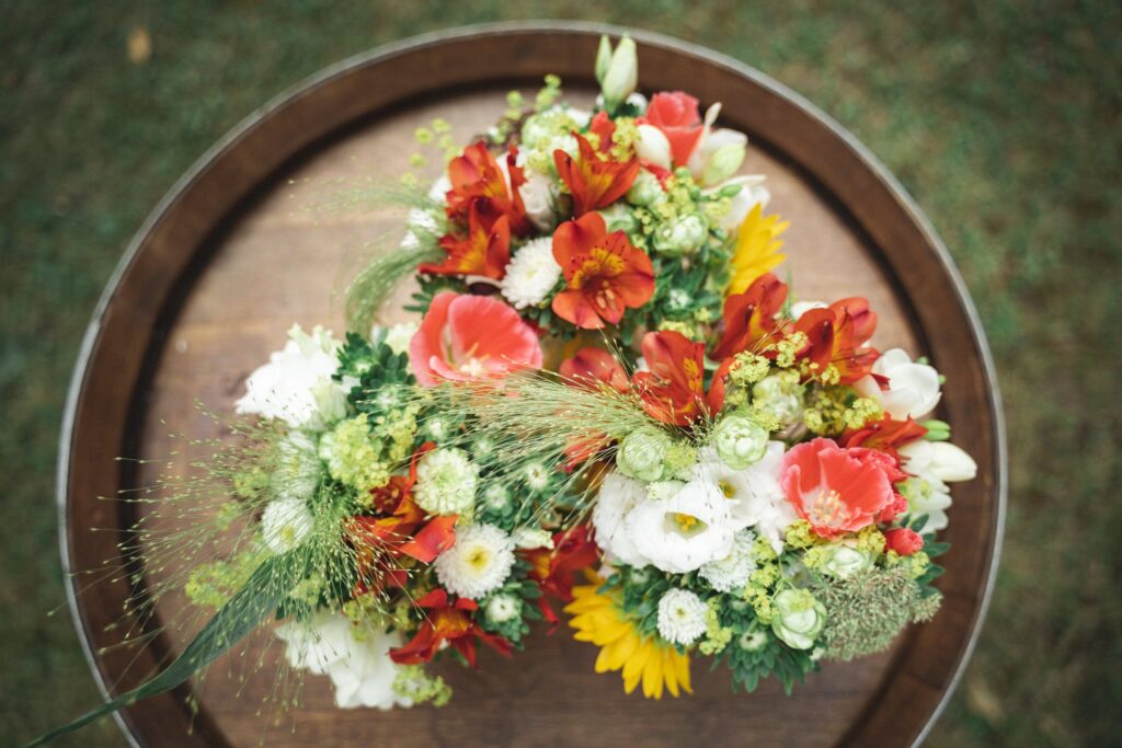 Un bouquet de fleurs rouges, blanches et jaunes posé sur un tonneau en bois, vu du dessus.