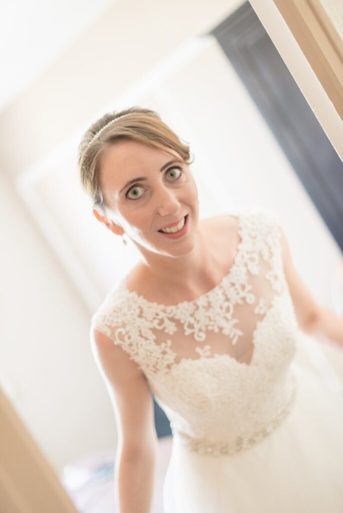 La mariée en robe de dentelle regarde l'objectif dans une pièce lumineuse.