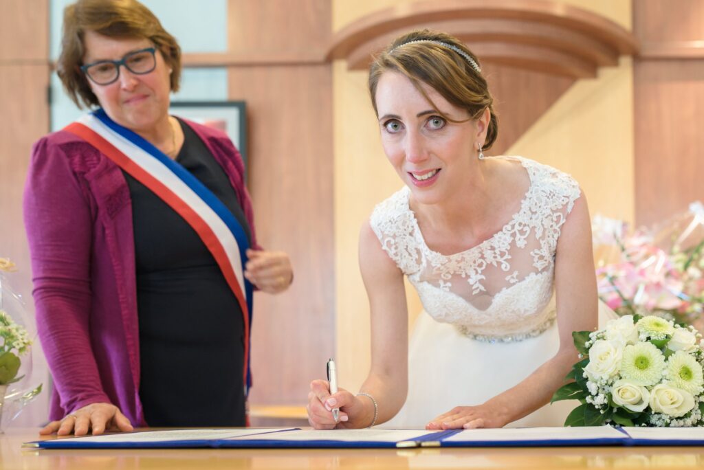 La mariée signe le registre à côté d'une élue qui porte l'écharpe tricolore.