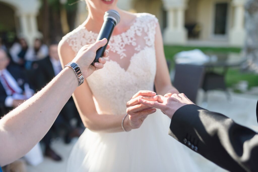 Gros plan sur l'échange des alliances, un micro tendu près de la robe de la mariée.
