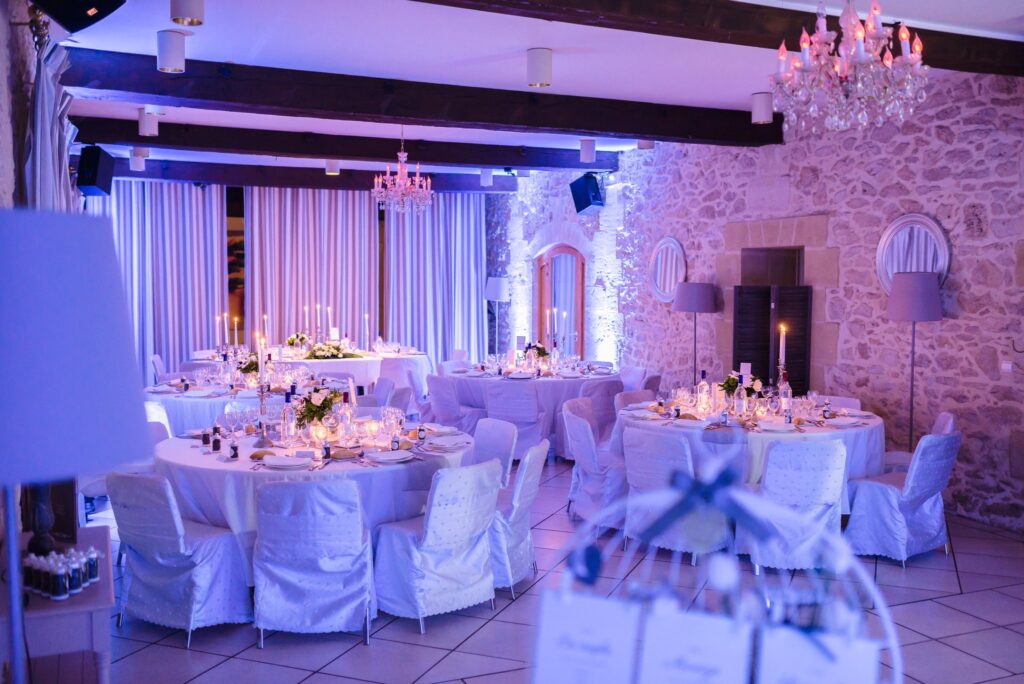 La salle de réception aux tables dressées, éclairée en bleu et violet.