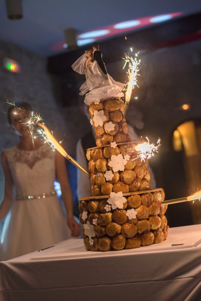 Une pièce montée de choux ornée de figurines et d'étincelles, avec un mannequin en robe blanche derrière.