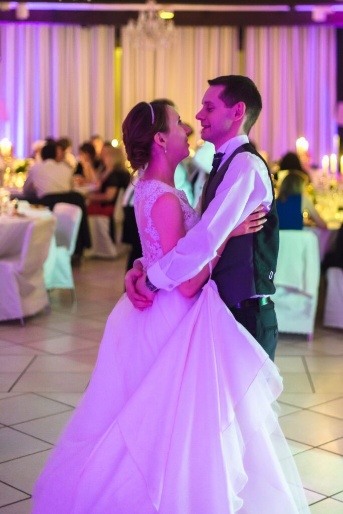 Les mariés enlacés dansent dans la salle, sous une lumière violette.